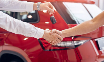 Car dealer with car keys shaking hand of client