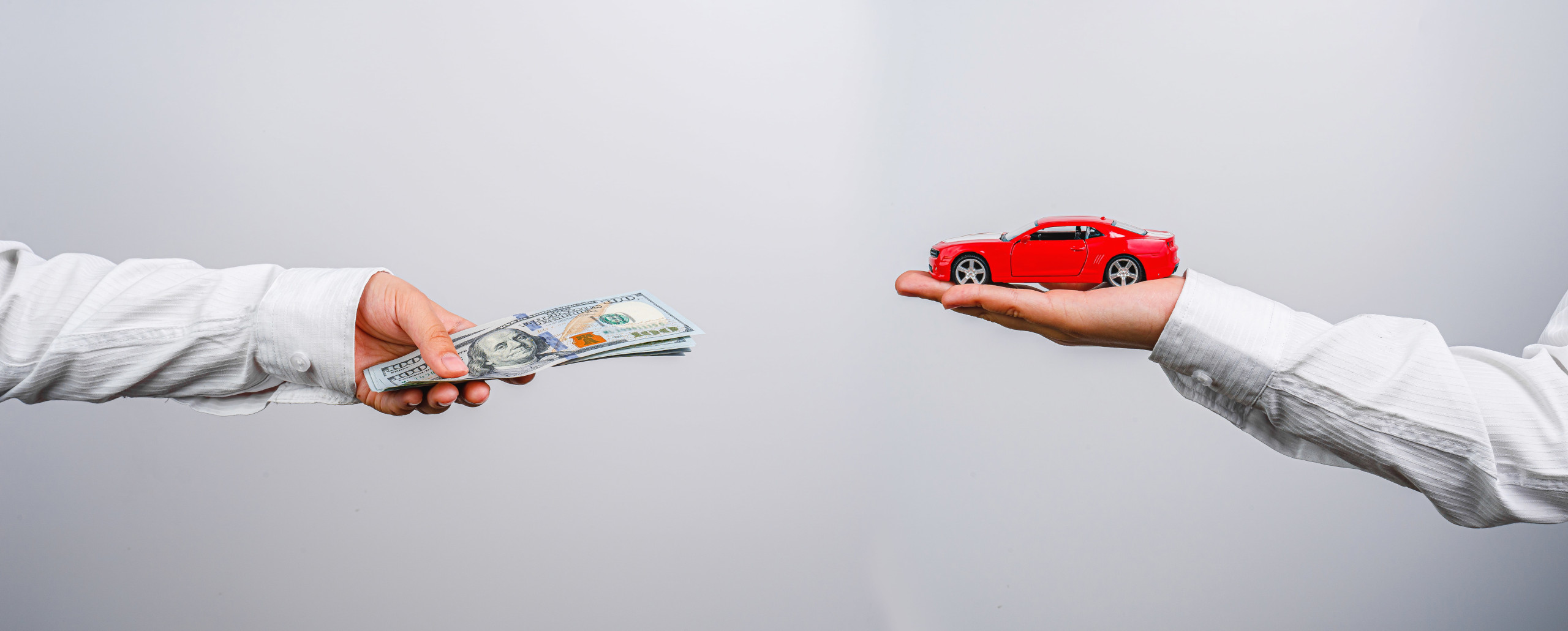 Two mens hands in corporate sleeves, one holding a red car, the other holding money
